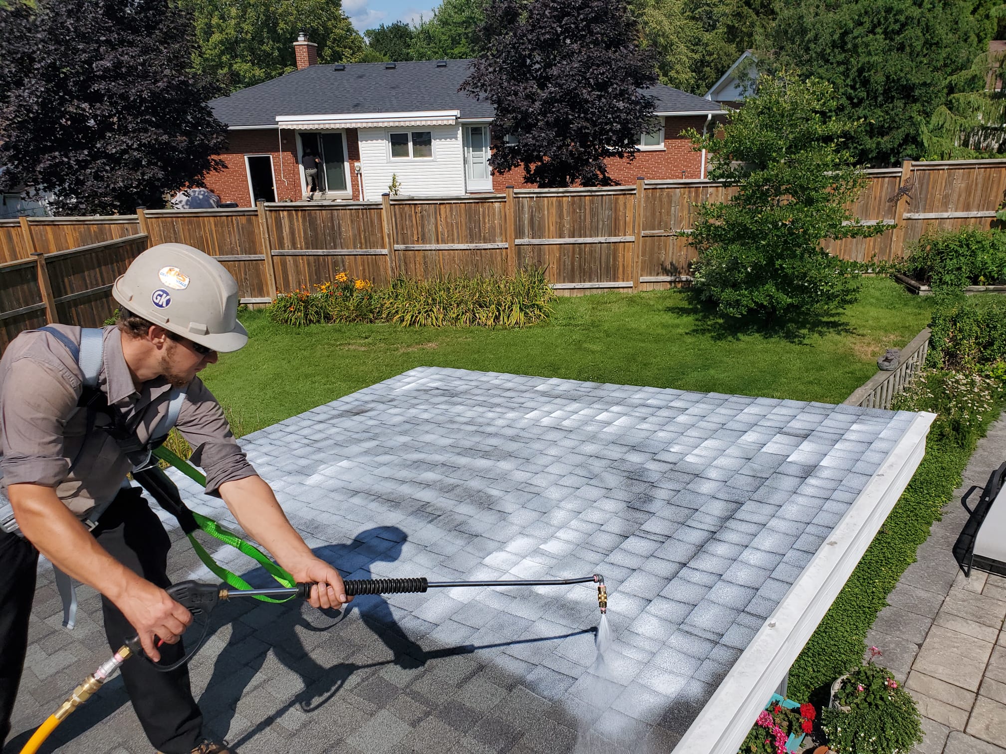 Roofer applying Reactiv8 plant-based rejuvenation spray to an aging asphalt shingle roof.